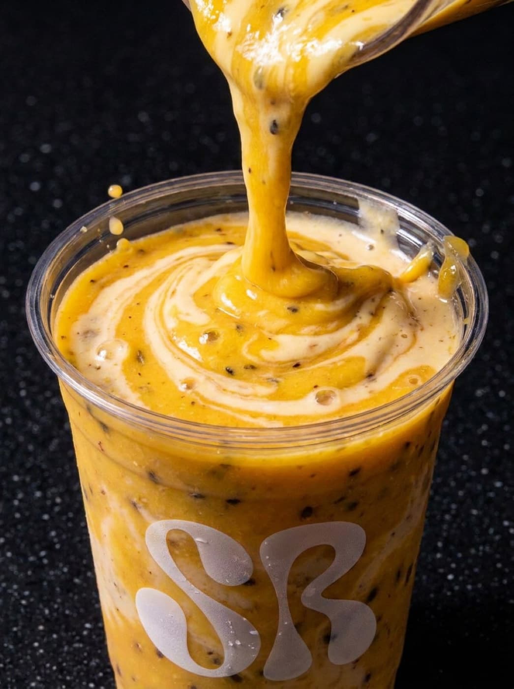 A mango shake being poured into a Shakeroom cup on a dark surface